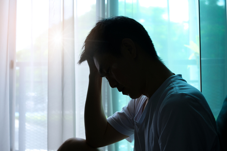 silhouette of a man sitting in the corner of a dark room with a severe headache